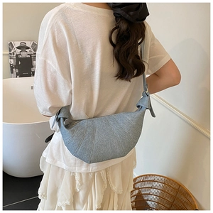Detail of light blue denim croissant bag with radial stitching and knotted strap