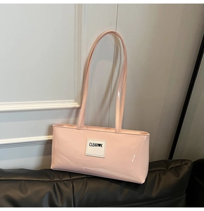 Close-up of pink glossy patent leather shoulder bag with logo patch on a black leather sofa