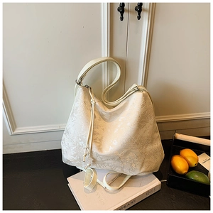 Close-up of cream floral jacquard hobo bag placed on a book in a lifestyle setting