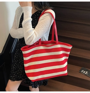 Detail of red and white striped knit tote bag with red leather handles shown in lifestyle setting