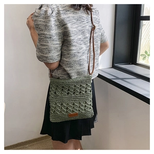 Detail of hand-woven grass green crossbody bag with leather strap and decorative patch