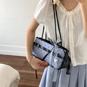 Detail of light blue polka dot shoulder bag with black leather buckle and bow accents