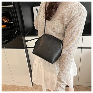 Detail of a minimalist black pebble leather crossbody shell bag worn in a modern setting