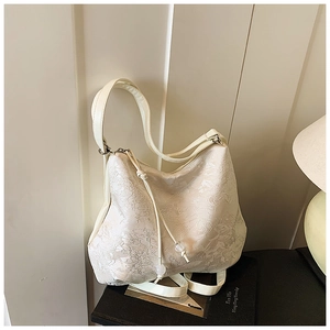 Close-up of beige shoulder bag with embossed floral pattern and decorative bead drawstring