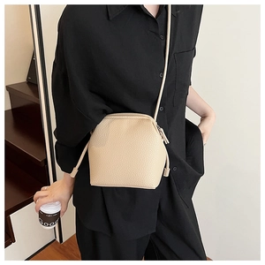 Detail of a beige lychee pattern leather crossbody bag worn on a black outfit