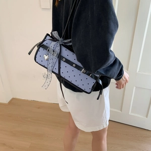 Detail of light blue polka dot baguette bag with bow and heart charm on a shoulder