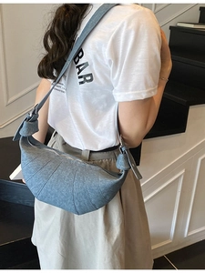 Denim blue large half-moon crossbody bag shown on model in a casual indoor setting