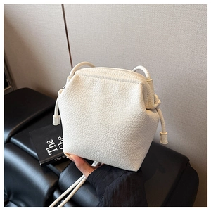 Détail d'un mini sac seau crème porté à la main montrant la texture cuir grainé