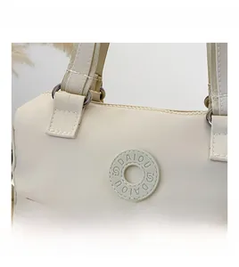 Close-up of cream nylon tote bag featuring round rubber logo and metal ring hardware