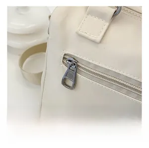 Detail shot of a beige nylon crossbody bag featuring a smooth silver metal side zipper