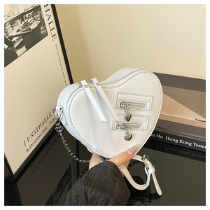 Detail of white heart-shaped crossbody bag with dual decorative zippers and chain strap