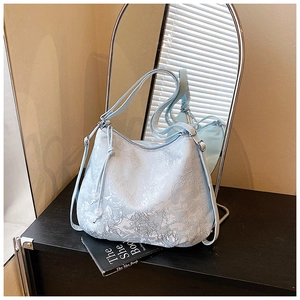 Detailed view of floral embossed pattern and drawstring beads on a light blue hobo bag