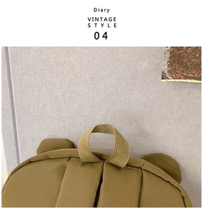 Detail of brown canvas backpack showing webbing handle and cute bear ear decorations