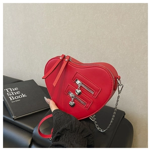 Detail of red heart-shaped leather crossbody bag with decorative zippers and chain