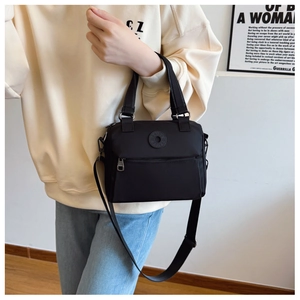 Close-up of black nylon crossbody bag with dual handles and circular logo detail
