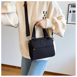 Detail of a black nylon crossbody bag featuring round logo and adjustable shoulder strap