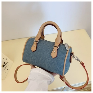 Detailed macro view of denim barrel bag with premium leather handles and silver hardware