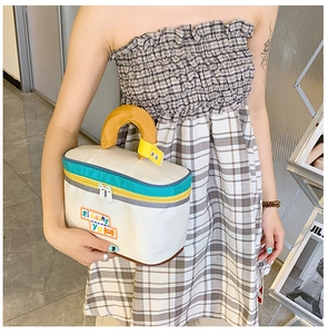 Detail view of large white cosmetics bag with yellow handle and cartoon logo patch
