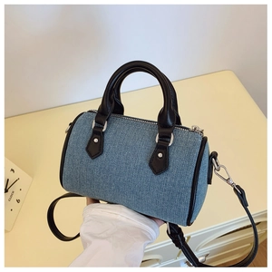 Detailed macro of blue denim cylinder mini Boston bag with black leather handle and trim