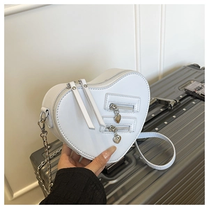 Detail of white heart-shaped crossbody bag featuring dual silver zippers and chain strap
