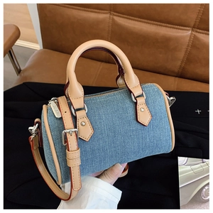 Detail of a mini denim Boston bag with tan leather trim and silver metal hardware