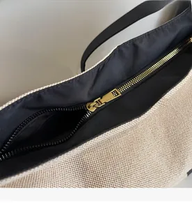 Macro view of smooth gold metal zipper and textured beige woven canvas bag detail