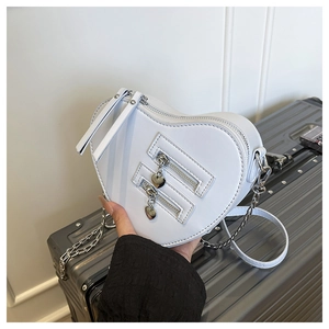 Detail of white heart-shaped bag with metal chain strap on a silver suitcase