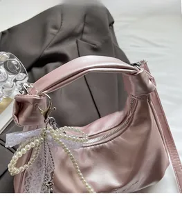 Detail of pink metallic handbag with knotted handle and decorative pearl lace bow