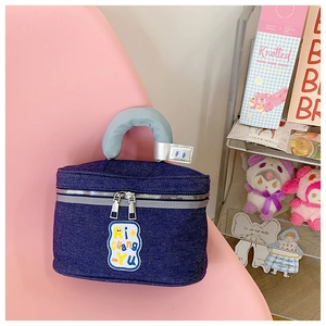 Detail of blue denim cosmetic bag with yellow embroidered letters and soft handle