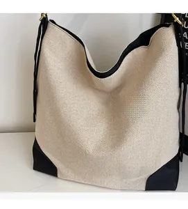 Detail view of large beige woven tote bag with black leather corners and gold hardware