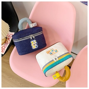 Close-up of portable house-shaped cosmetic bags on chair showing dual zipper and logo detail