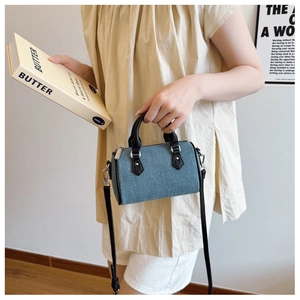 Detailed shot of a blue denim mini Boston bag with black leather handles and silver hardware