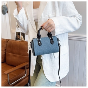 Close-up of a stylish mini barrel bag in blue denim with black leather straps and silver hardware