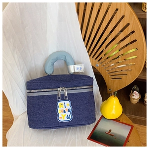 Detailed view of blue denim makeup bag with padded handle and stylish logo patch