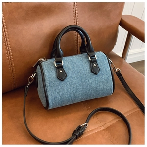 Detail of blue denim pillow bag with black leather trim on a vintage leather sofa