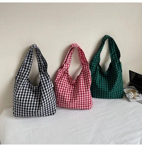 Flat lay of red, black, and green checkered canvas tote bags with lifestyle props
