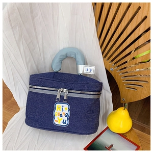 Detail of dark blue denim makeup bag with embroidered patch and silver metal dual zippers