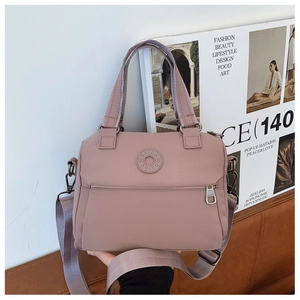 Detail of dusty pink nylon shoulder bag with circular logo and front zipper on sofa