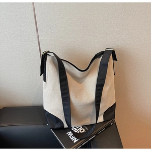 Detail of canvas tote bag showing contrast black base and shoulder strap on leather sofa