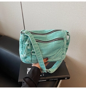 Detail of mint green denim crossbody bag showing multiple functional zippers and texture