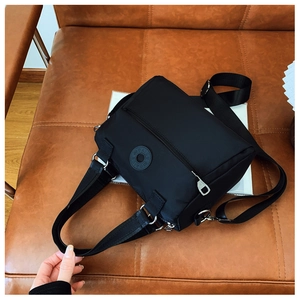 Detail view of the durable nylon fabric texture and circular logo on the black shoulder bag