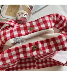 Close-up of red plaid canvas tote bag featuring magnetic buckle closure and durable cotton lining