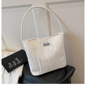 Close-up of a pleated white fabric shoulder bag with a minimalist blue brand label