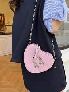 Pink heart-shaped crossbody bag with silver chain and dual zippers on a model
