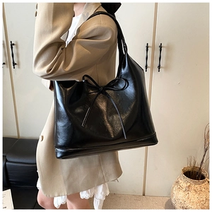 Detail of black wax leather tote bag with bow accent shown on a model for scale