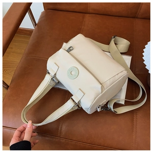 Detail view of the beige nylon crossbody bag featuring a round logo and wide strap