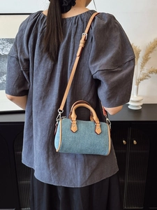 Mini denim Boston pillow bag with leather trim worn as a stylish crossbody handbag