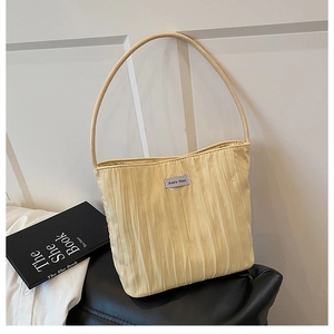Detail of light yellow pleated canvas tote bag featuring an embroidered brand label