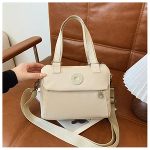 Detail of a beige nylon crossbody bag featuring a round logo patch and wide strap