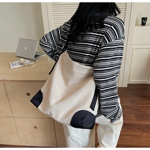 Detail view of the large beige canvas tote bag with black contrast trim on a shoulder